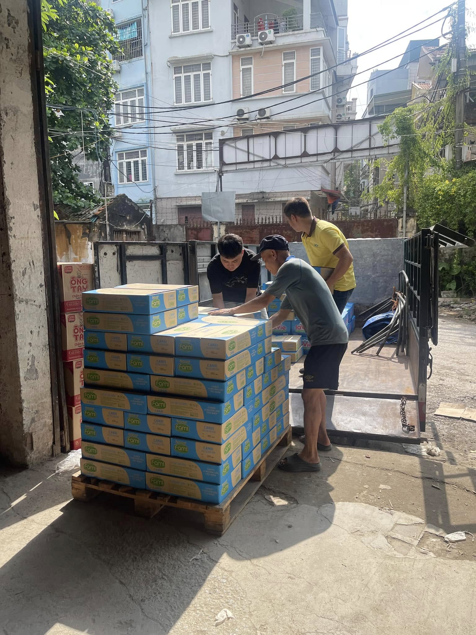 Ba người đàn ông đang bốc xếp thùng hàng Fami từ xe tải xuống pallet trước cửa kho