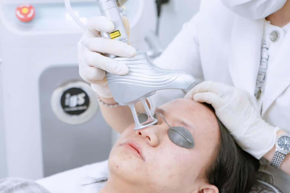 Bác sĩ dùng máy laser điều trị da mặt cho khách hàng đeo kính bảo hộ trong phòng khám